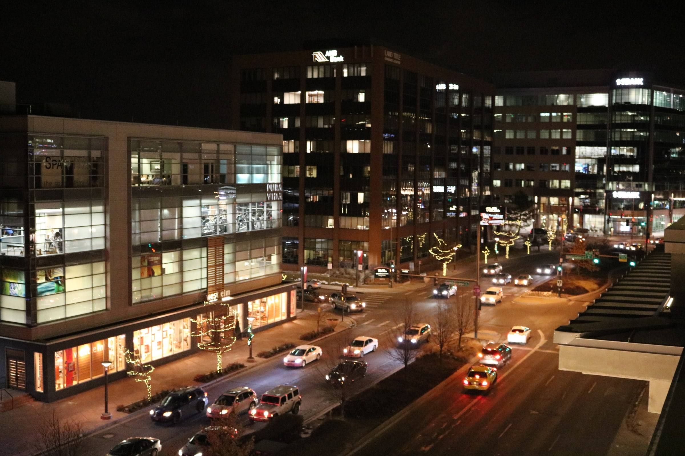 Lit storefronts and glass-fronted buildings along 1st Avenue at the edge of Cherry Creek North